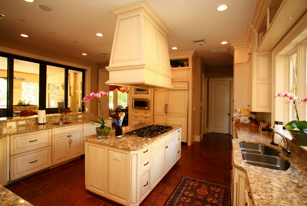 Kitchen with a cream painted hood, granite counters, terracotta tile floor, and a center island cooktop