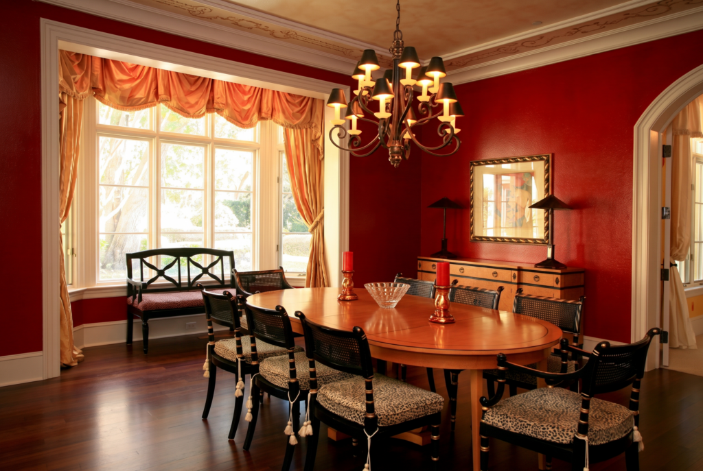Dining room with a bay window, iron chandelier, and deep red walls