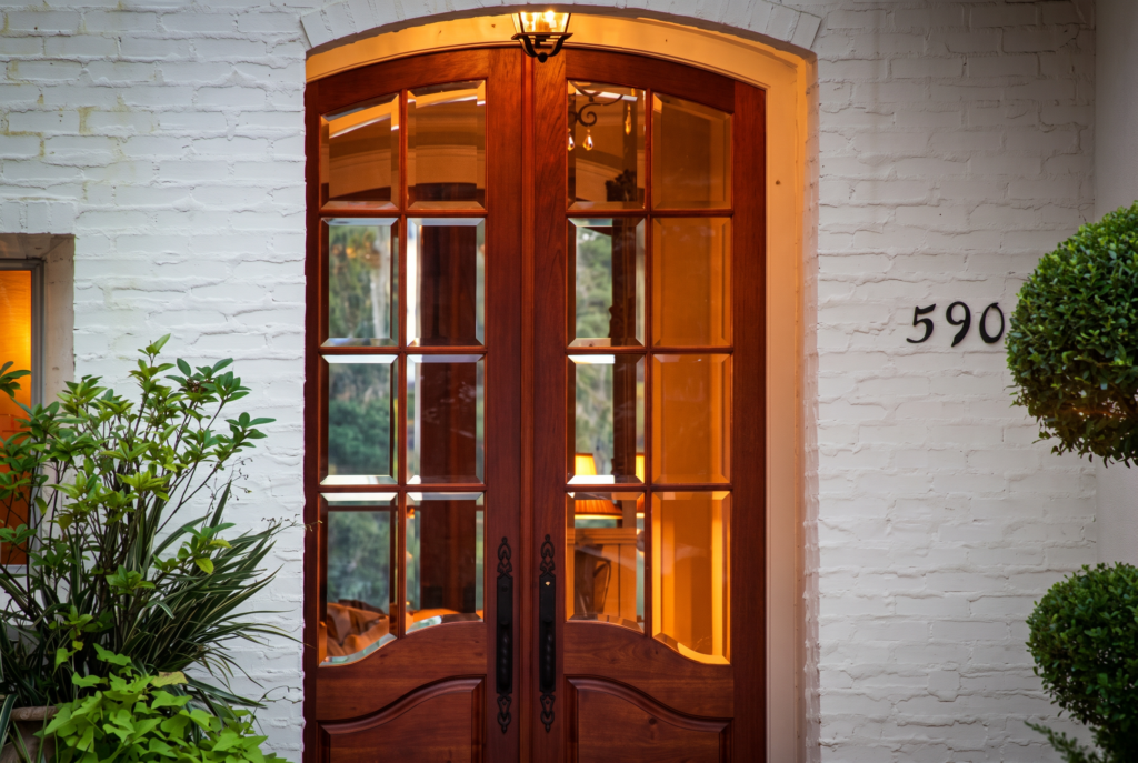 Arched mahogany French entry doors with divided lights, set into a whitewashed brick facade