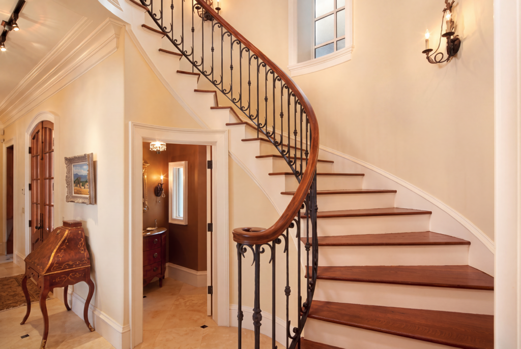 Curved staircase with a wrought iron rail, wood treads, and an iron sconce on a plaster wall