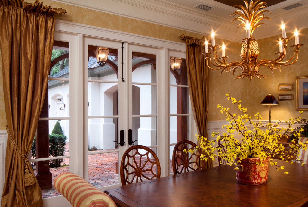 Dining room with an iron and gilt chandelier, floor-to-ceiling French doors, and a view to the covered veranda