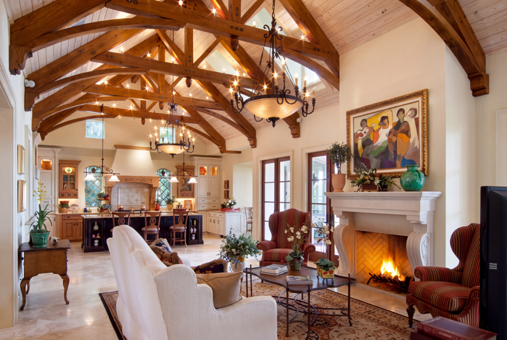 Great room under a vaulted ceiling with curved timber trusses, opening to the kitchen past a stone fireplace