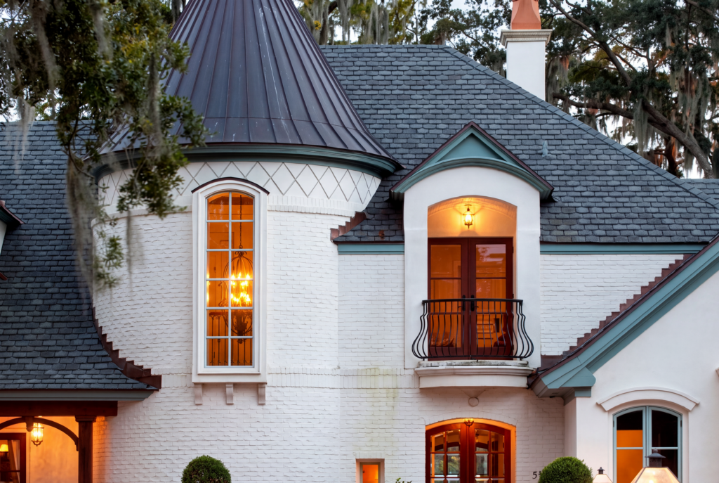 Conical slate turret with a copper-topped roof and wrought iron balcony on a whitewashed brick French Country home