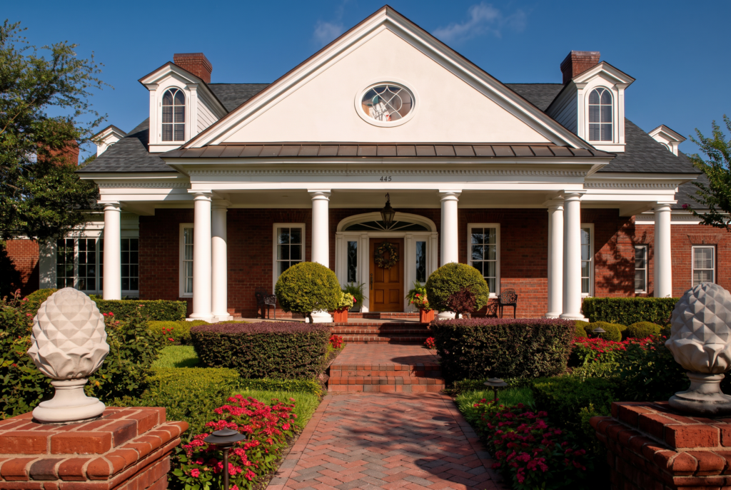 Front entry with a brick paver walk, twin columned porticos, dormers, and carved pineapple finials on brick piers