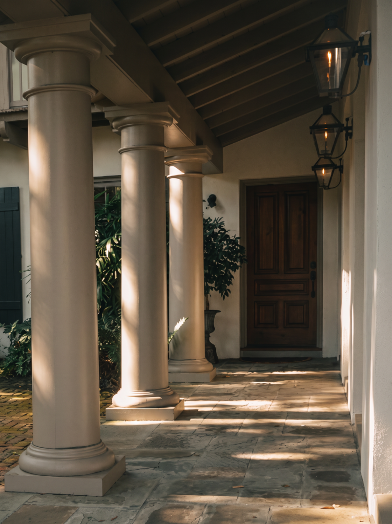 Entry loggia with Tuscan columns, gas lanterns, an exposed rafter ceiling, and a mahogany door