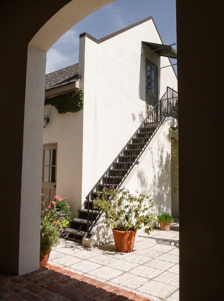Arched opening onto a courtyard with an exterior iron stair and a brick-capped stucco wall