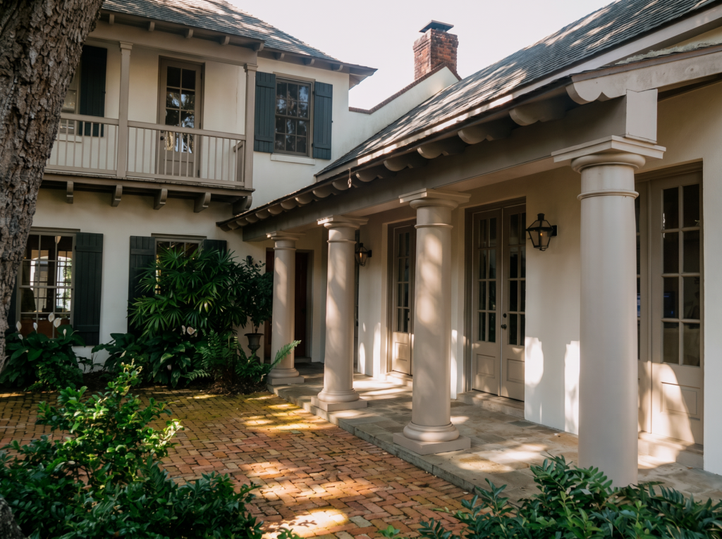 Loggia with Tuscan columns, a second-story balcony above, and a brick paver courtyard