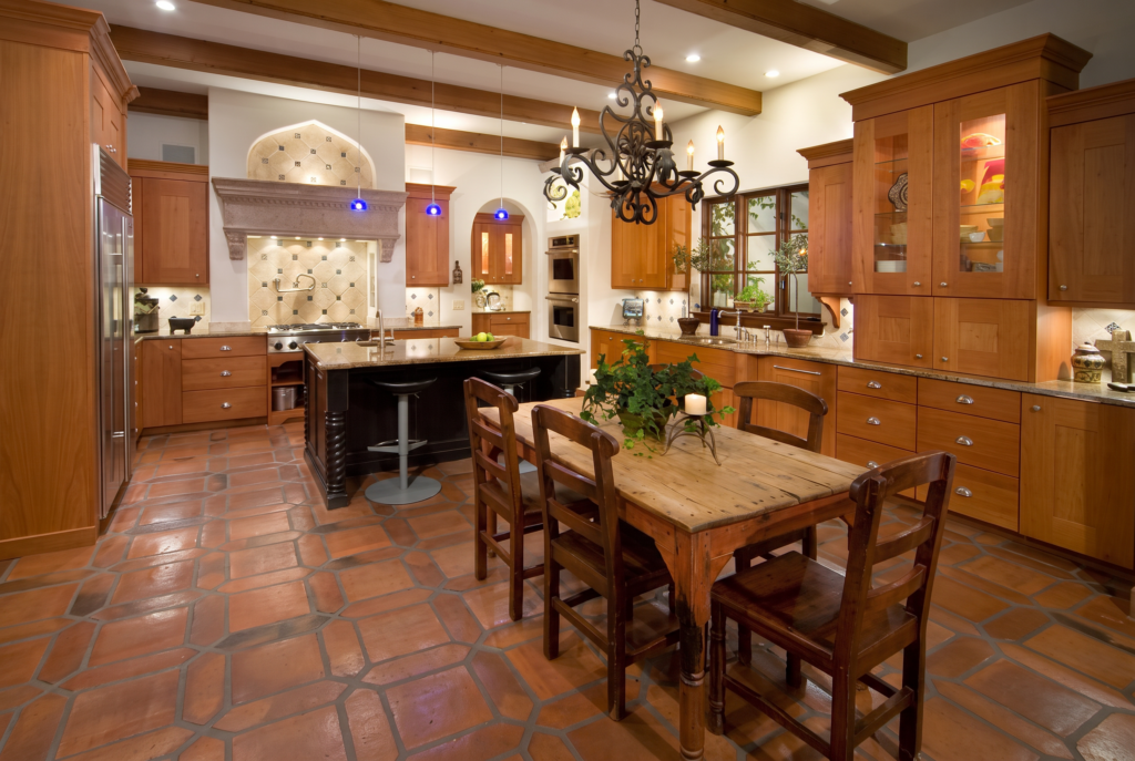Kitchen with a plaster hood over an arched tiled alcove, wood cabinetry, terracotta floors, and a farmhouse table